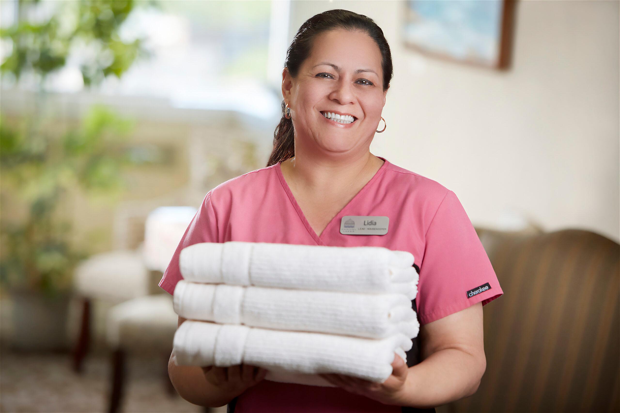 A smiling Capitol Lakes healthcare worker holds a stack of towels.